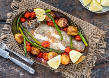 su tavolo di legno sotto tavolo stile bohémien con un piatto con sogliola al forno, patate, asparagi, pomodorini con alcune fette di limoni . Sulla sinistra forchetta e coltello
