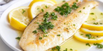 su tavolo, primo piano di un piatto bianco con una sogliola alla mugnaia con prezzemolo e fette di limone
