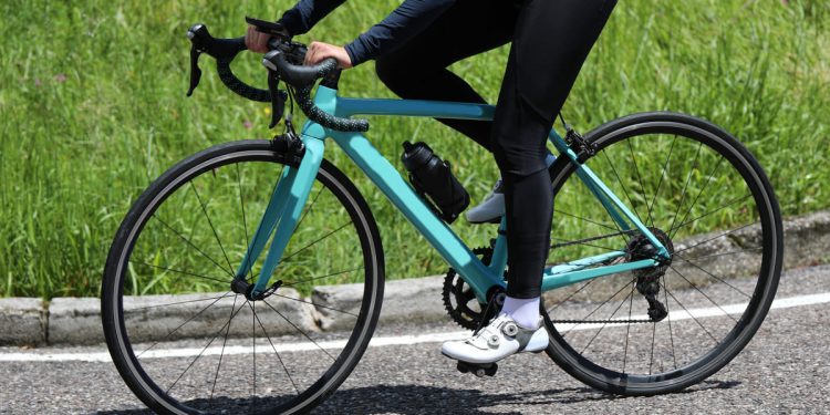 Bici da corsa verde acqua in primo piano su sfondo una strada, con telaio aerodinamico e dettagli tecnici visibili