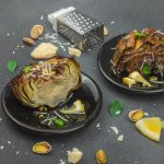 su tavolo di marmo, 2 piatti neri con carciofi bolliti, attorno pistacchi, fette di limone, grattugia e parmigiano reggiano
