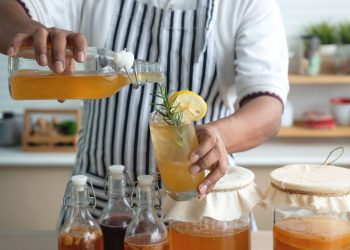 come fare kombucha: uomo in cucina con grembiule che sta preparando kombucha in casa e riempie i bicchieri