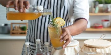 come fare kombucha: uomo in cucina con grembiule che sta preparando kombucha in casa e riempie i bicchieri