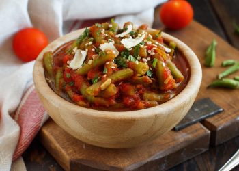 su tavolo, tagliere con ciotola in marmo con fagiolini all'uccelletto con alcuni fagiolini lavati e tagliati e dietro pomodorini