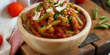su tavolo, tagliere con ciotola in marmo con fagiolini all'uccelletto con alcuni fagiolini lavati e tagliati e dietro pomodorini