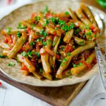 su tavolo apparecchiato tagliere con sopra un piatto con fagiolini in umido con pomodorini e prezzemolo e una forchetta sulla destra peperoncini