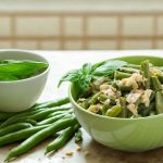 su tavolo da cucina, ciotola verde con fagiolini lessi e parmigiano, accanto un'altra ciottola con basilico e a destra fette di pizza