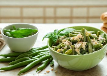 su tavolo da cucina, ciotola verde con fagiolini lessi e parmigiano, accanto un'altra ciottola con basilico e a destra fette di pizza