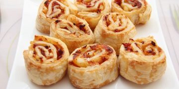 in primo piano un piatto bianco con delle girelle di pasta sfoglia farcite con prosciutto cotto e formaggio