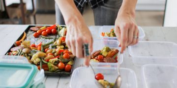 donna in casa sul tavolo di cucina sta preparando il meal prep per la settimana quindi divide in diversi contenitori il cibo per i pasti successivi