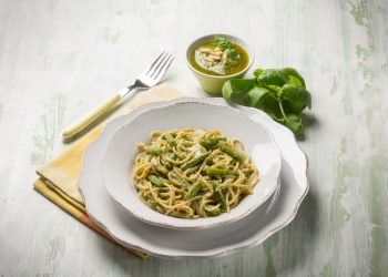 su tavolo bianco apparecchiato piatto bianco con pasta con fagiolini dietro basilico e accanto forchetta gialla e tovagliolo giallo