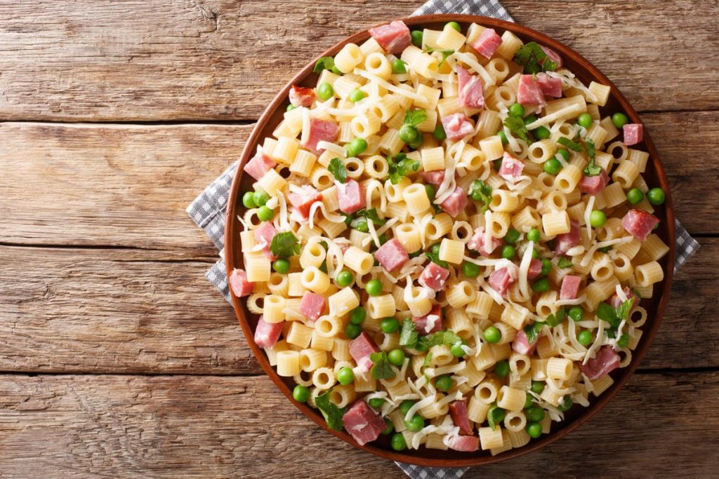 in primo piano un piatto di pasta con prosciutto cotto e piselli