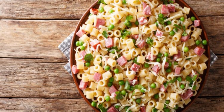 in primo piano un piatto di pasta con prosciutto cotto e piselli