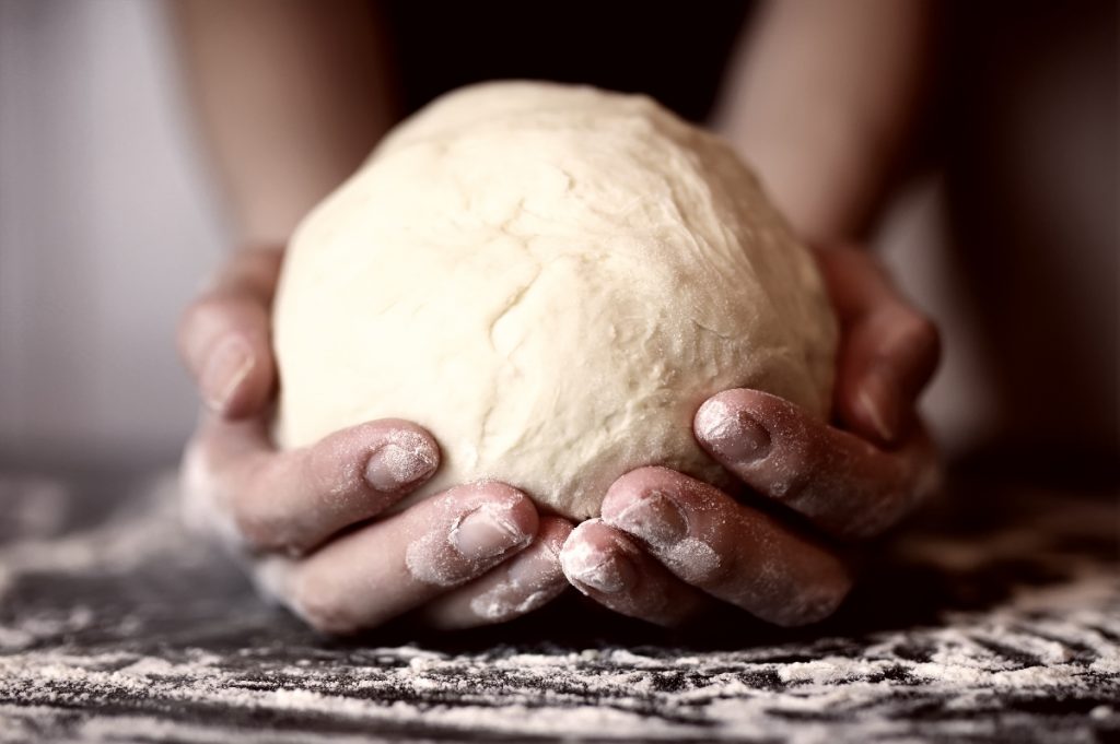 primo piano di mani di una donna che tiene in mano una palla di pasta matta dopo averla lavorata