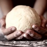 primo piano di mani di una donna che tiene in mano una palla di pasta matta dopo averla lavorata