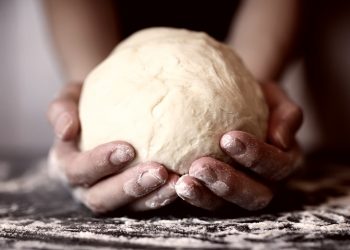primo piano di mani di una donna che tiene in mano una palla di pasta matta dopo averla lavorata