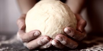 primo piano di mani di una donna che tiene in mano una palla di pasta matta dopo averla lavorata