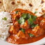 primo piano di un piatto bianco con riso basmati, pollo tikka masala e pane naan