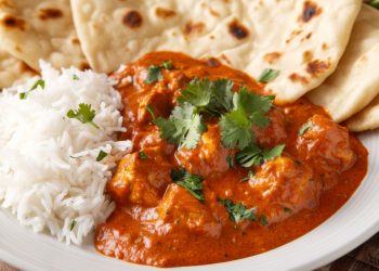 primo piano di un piatto bianco con riso basmati, pollo tikka masala e pane naan