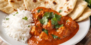primo piano di un piatto bianco con riso basmati, pollo tikka masala e pane naan