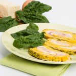in primo piano un piatto verde chiaro con rotolo di frittata decorato con una foglia di spinacino