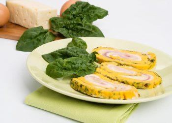 in primo piano un piatto verde chiaro con rotolo di frittata decorato con una foglia di spinacino
