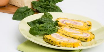 in primo piano un piatto verde chiaro con rotolo di frittata decorato con una foglia di spinacino