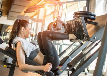 donna in palestra con asciugamano sulle spalle esegue con scheda palestra esercizio con la leg press per tonificare le gambe
