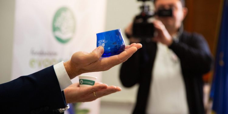una mano in primo piano mostra un vasetto blu con il logo eccebio, un cameraman filma sullo sfondo