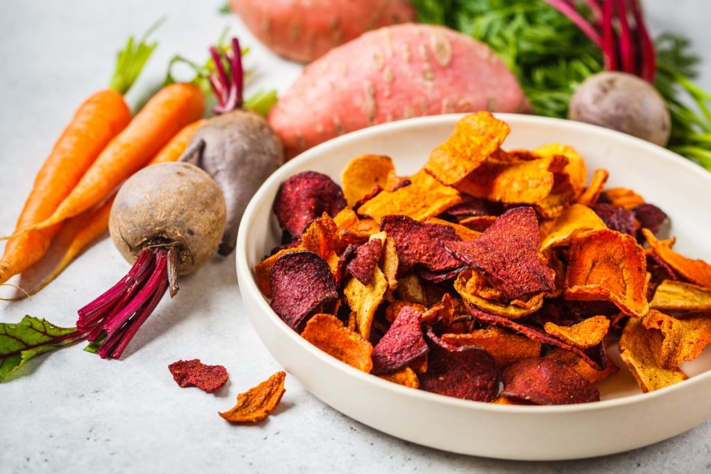 Chips di carote croccanti: la ricetta al forno e varianti 3 su tavolo piatto con chips di carote e barbabietole con attorno carote e barbabietole