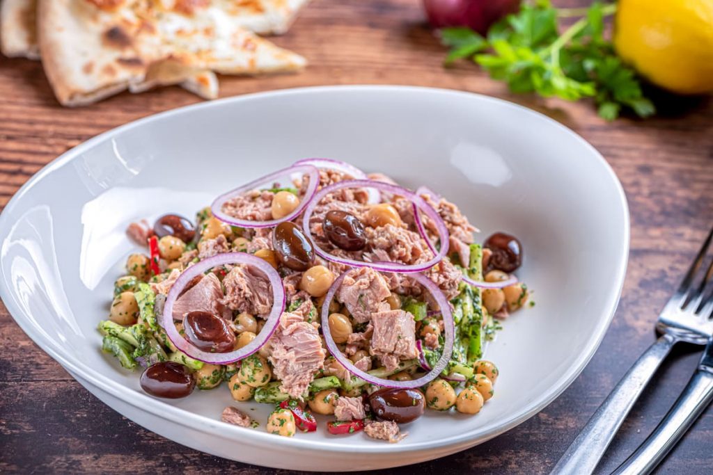 Insalata di ceci e tonno servita in un piatto fondo, con cipolla e olive taggiasche
