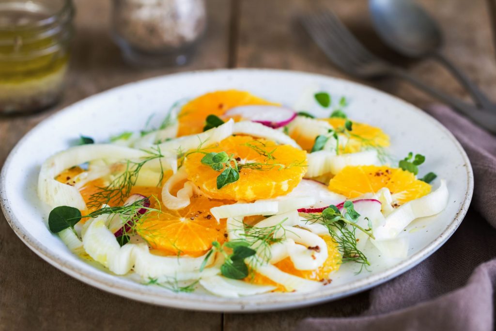 in primo piano su un piatto piano bianco una gustosa insalata di finocchi e arance, perfetta come contorno o antipasto