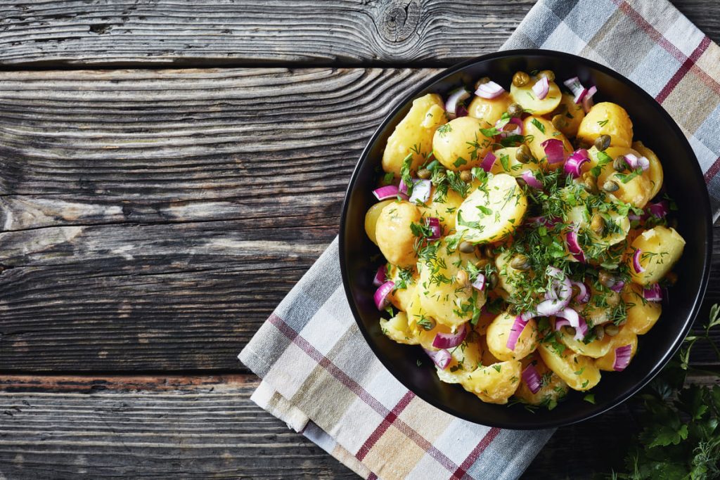 in primo piano su un piatto fondo nero dell'insalata di patate con cipolle rosse e prezzemolo