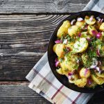 in primo piano su un piatto fondo nero dell'insalata di patate con cipolle rosse e prezzemolo