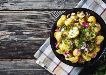 in primo piano su un piatto fondo nero dell'insalata di patate con cipolle rosse e prezzemolo