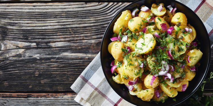 in primo piano su un piatto fondo nero dell'insalata di patate con cipolle rosse e prezzemolo