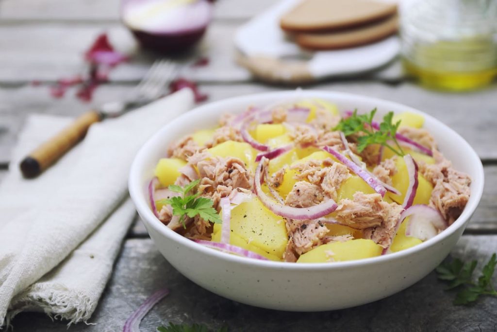 in primo piano, in un piatto fondo bianco un'insalata patate e tonno con cipolla rossa
