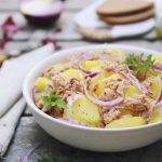 in primo piano, in un piatto fondo bianco un'insalata patate e tonno con cipolla rossa