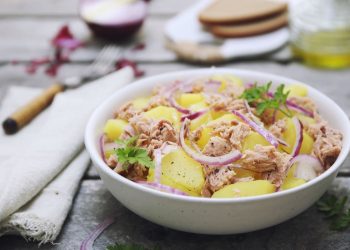 in primo piano, in un piatto fondo bianco un'insalata patate e tonno con cipolla rossa