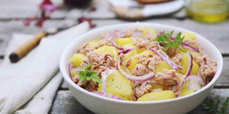 in primo piano, in un piatto fondo bianco un'insalata patate e tonno con cipolla rossa