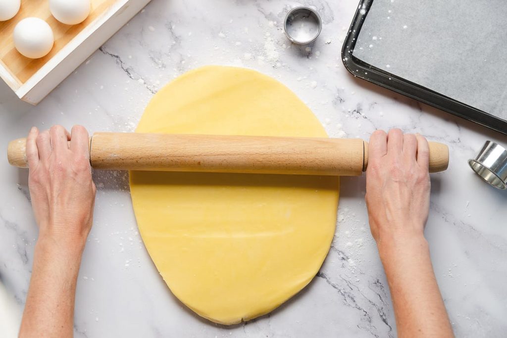 in primo piano la pasta frolla senza burro mentre viene stesa con un mattarello.