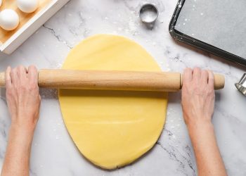 in primo piano la pasta frolla senza burro mentre viene stesa con un mattarello.