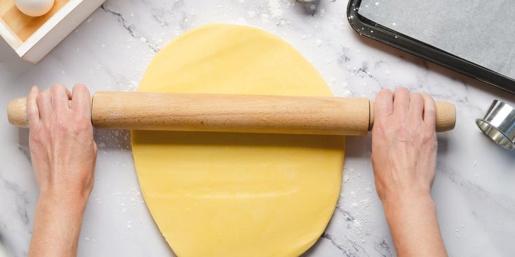in primo piano la pasta frolla senza burro mentre viene stesa con un mattarello.