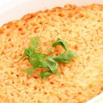 in primo piano in una pirofila di forma ovale del riso al forno guarnito con qualche foglia di basilico