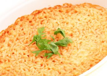 in primo piano in una pirofila di forma ovale del riso al forno guarnito con qualche foglia di basilico