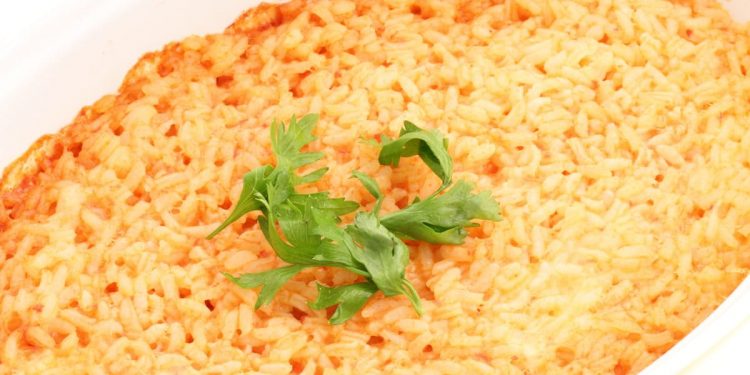 in primo piano in una pirofila di forma ovale del riso al forno guarnito con qualche foglia di basilico