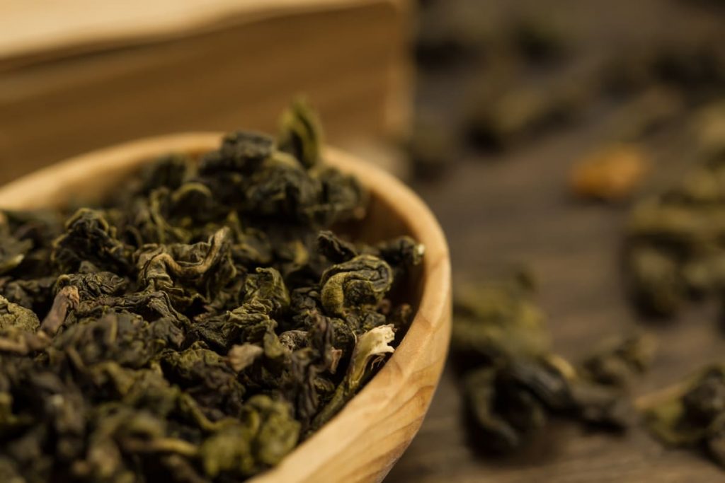Tè oolong: la bevanda orientale ricca di benefici che stimola il metabolismo 1 in primo piano, in una ciotola di legno delle foglie di tè oolong essiccate e arrotolate