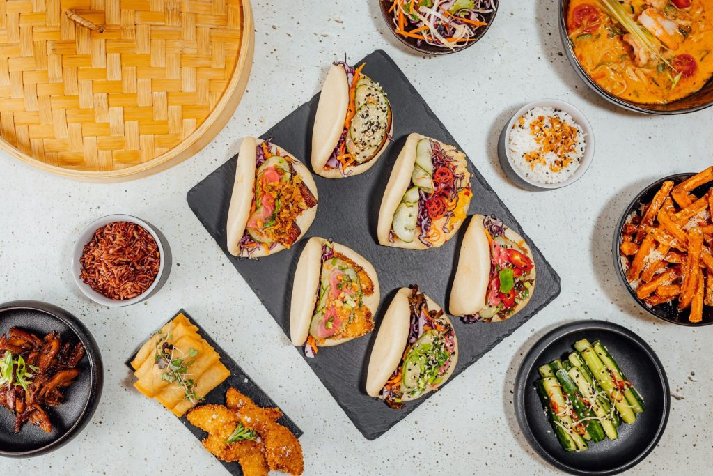 su tavolo di marmo: tagliere nero con 6 bao buns ripieni di verdure, attorni verdure e spezie