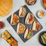 su tavolo di marmo: tagliere nero con 6 bao buns ripieni di verdure, attorni verdure e spezie