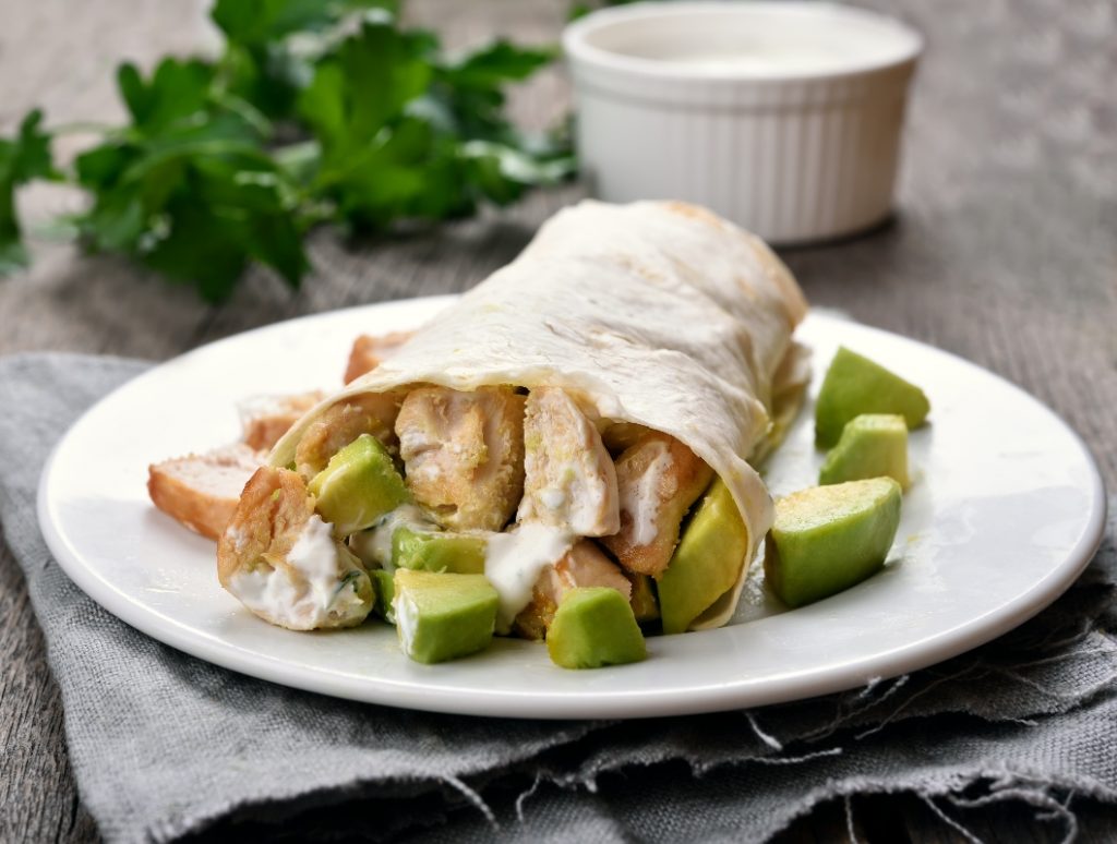 primo piano di un piatto bianco sul tavolo con burrito di pollo e avocado