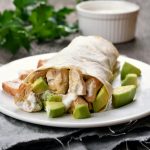 primo piano di un piatto bianco sul tavolo con burrito di pollo e avocado
